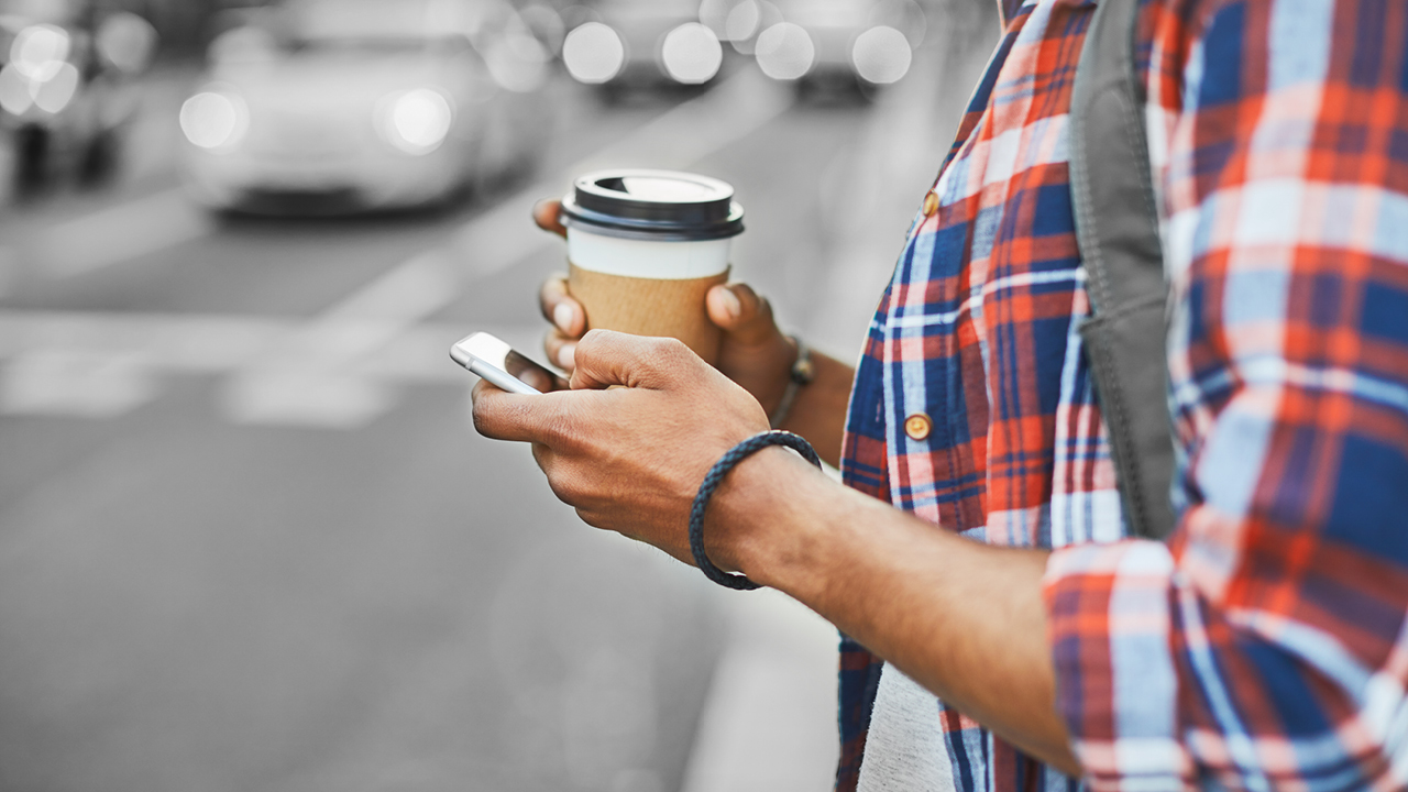 A man holding a cup of coffee and using mobile; image used for HSBC Australia mobile banking.