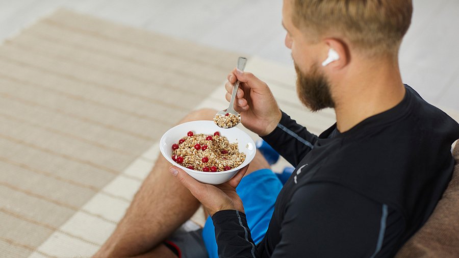 Junger Mann in Sportkleidung sitzt mit dem Rücken zur Kamera und isst Müsli