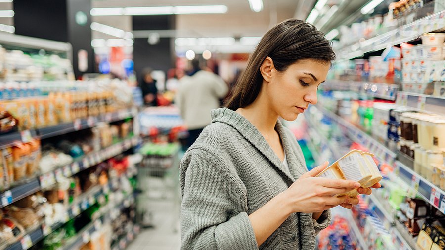 Frau vor einem Supermarkregal betrachtet eine Yoghurtpackung