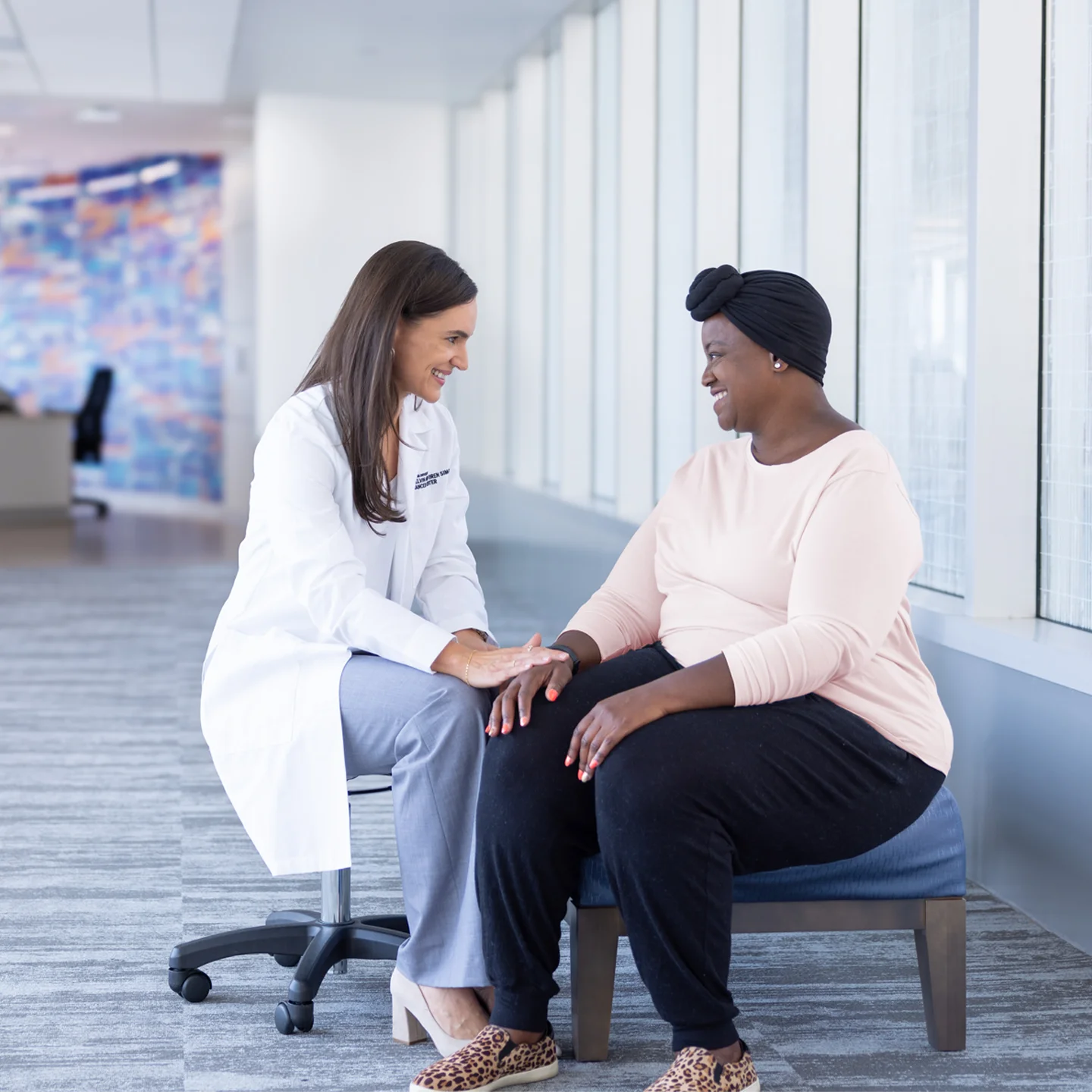 Dr. Tarah Ballinger, MD, sits with a black female breast cancer patient in the bright lobby of the Simon Cancer Center.