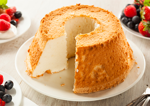 Freshly cut angel cake on a white plate with berries in the background