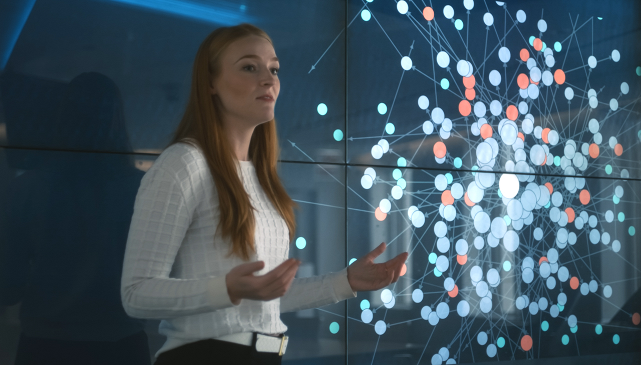 A business professional giving a presentation in front of a data screen