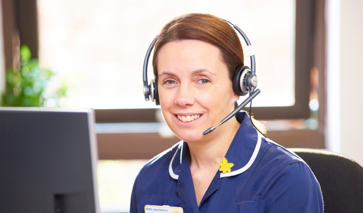 Marie Curie Support Line Officer sits at a desk with a headset on, ready to take a call. 