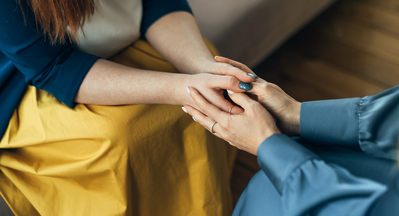 Two women sitting across from each other with their hands embraced