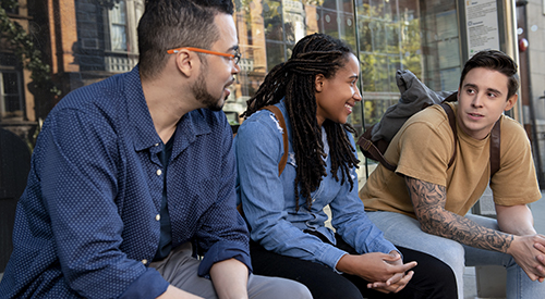 Three Veterans with backpacks sitting down on a bench on a campus.