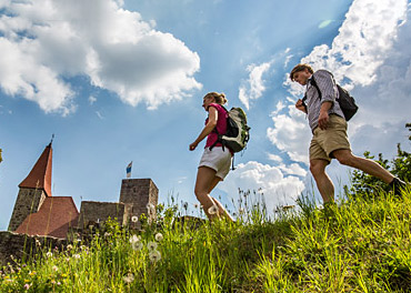 Das Bild zeigt 2 Wanderer auf einer Wiese vor einer Burgruine