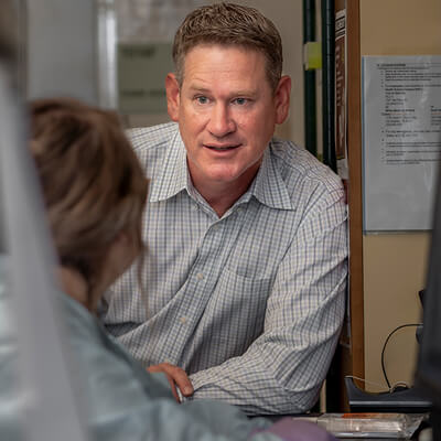 Photo: Dr. Christopher Haiman wearing a white and grey plaid shirt talking to a colleague at the University of Southern California