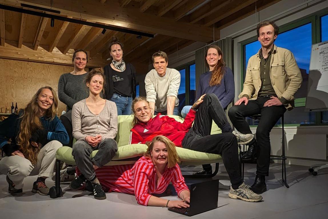 Gruppenfoto von neun Menschen um ein Sofa herum. Klick führt zu Großansicht in neuem Fenster, schließen per ESC.