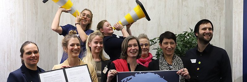 Menschen halten ein Dokument und ein Plakat in die Kamera.