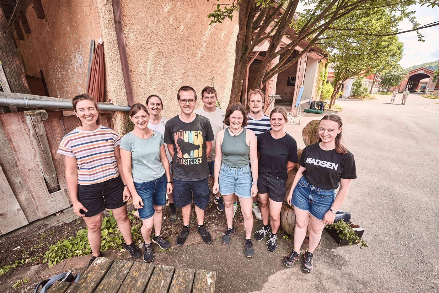 Gruppenbild von 9 Menschen, die nebeneinander stehen. Klick führt zu Großansicht in neuem Fenster, schließen per ESC.