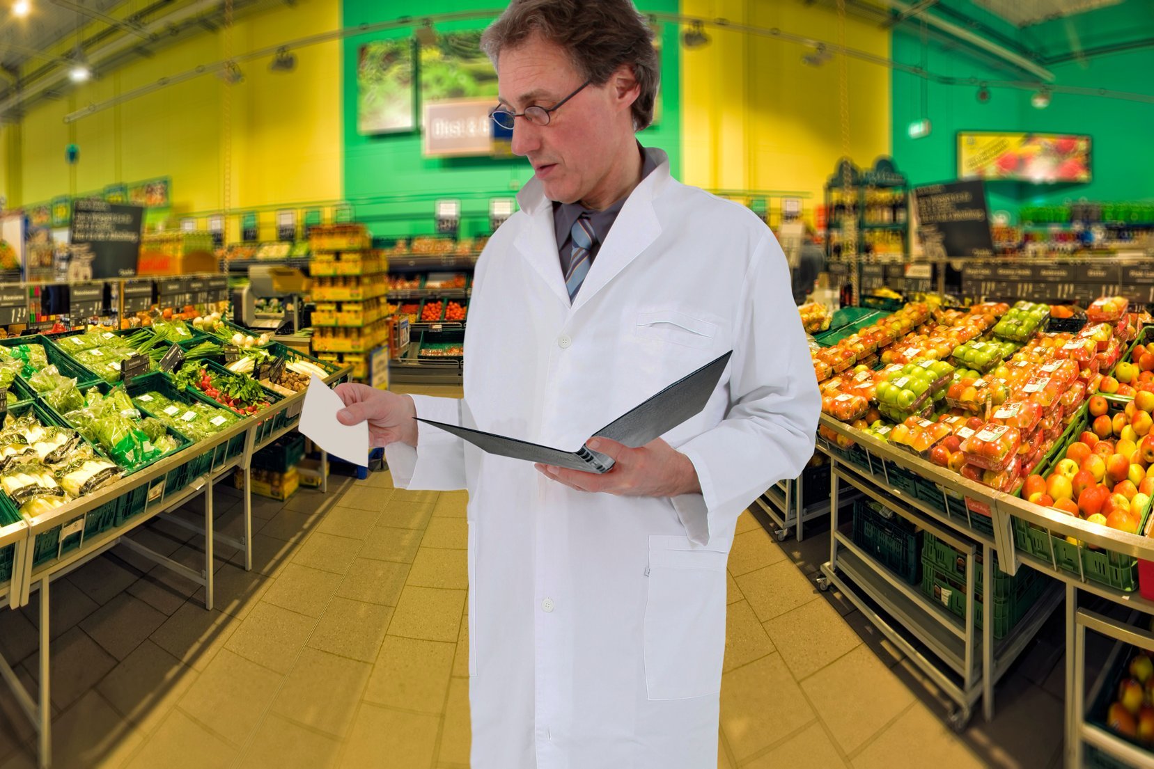 Mann im weißen Kittel und Mappe in der Hand steht im Supermarkt.