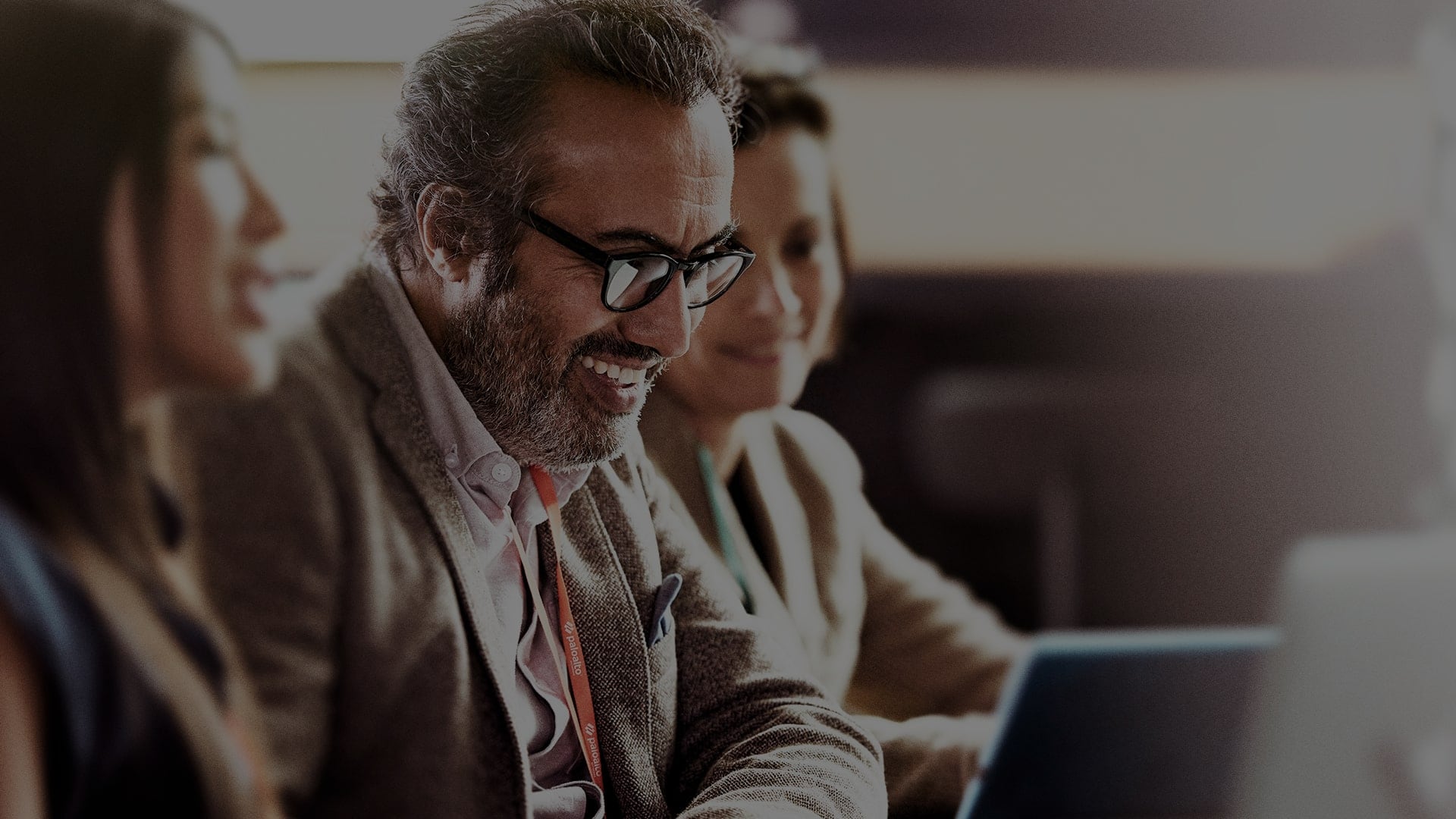 Man with glasses using laptop flanked by colleagues