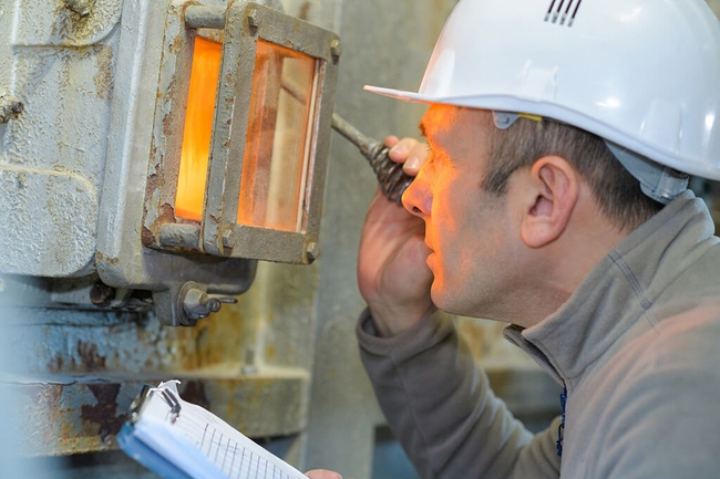 Mann schaut durch das Schauglas einer Industrieverbrennungsanlage