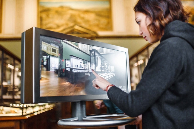 Junge Frau bedient einen Touchscreen-Monitor im Museum 