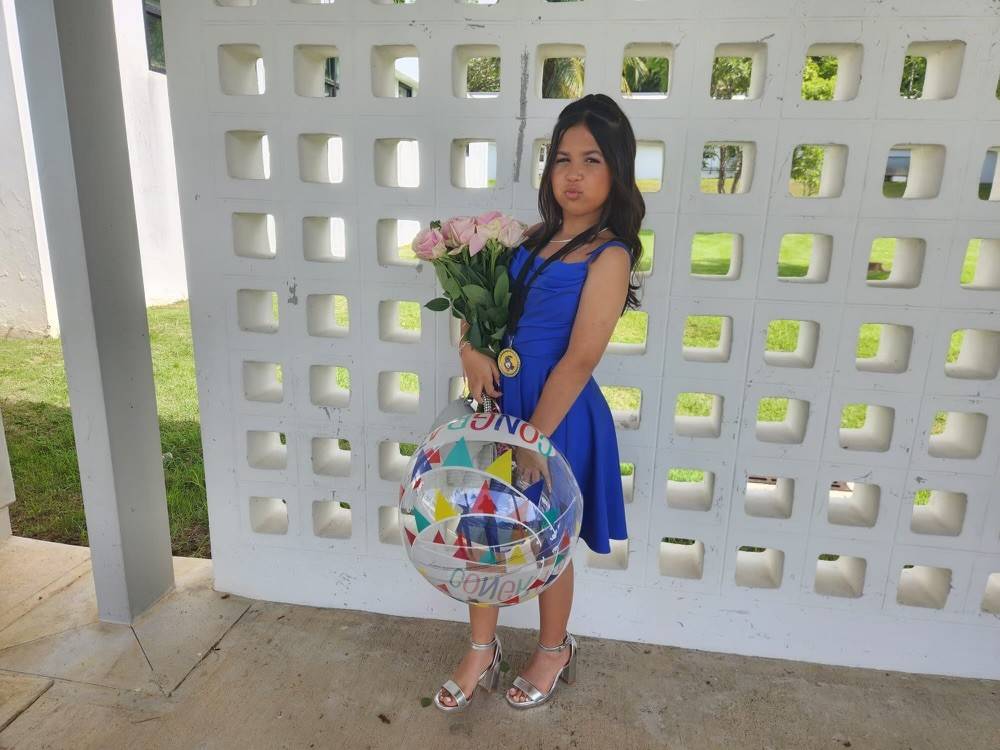 Angelique Delgado is wearing a beautiful blue dress and holding flowers as she poses for the camera