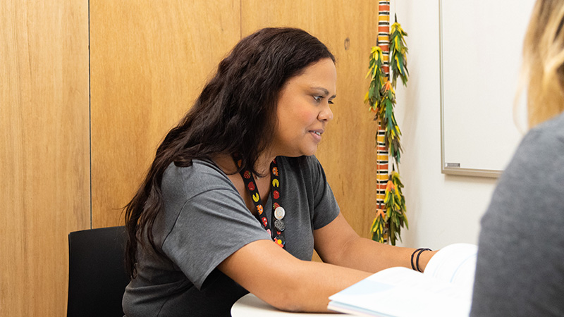 a woman wearing a lanyard sitting at a desk in the rmit ngarara willim centre