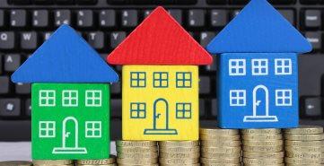 Image of wooden toy houses stood on piles of one pound coins of increasing height, with a computer keyboard in the background