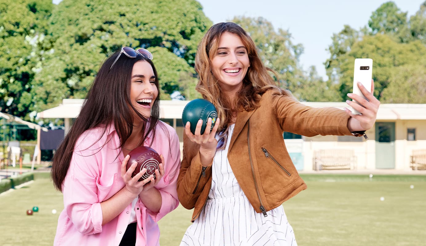 Two women smiling and posing for a selfie while holding a bowling ball.