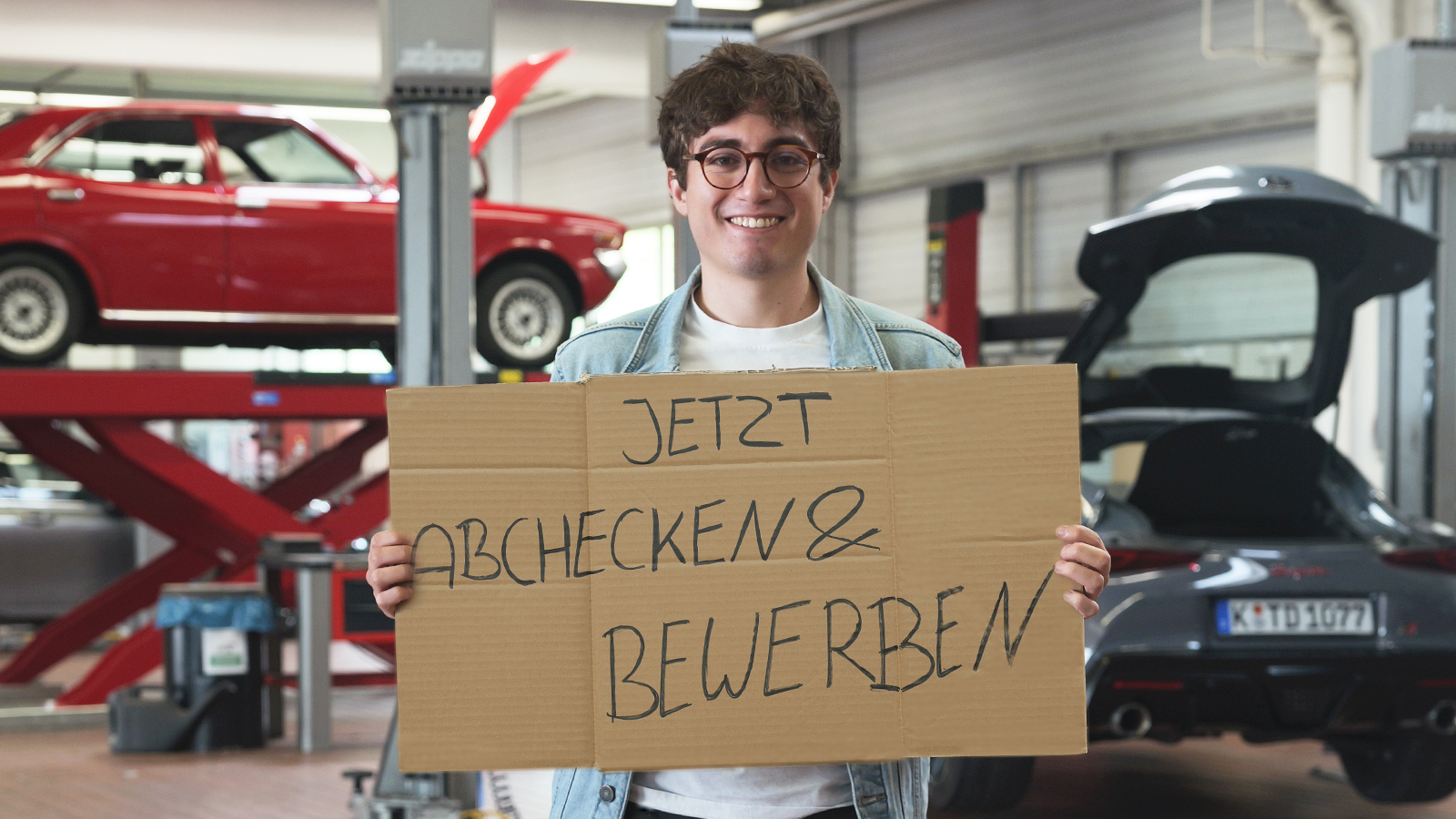 Ein Mann mit einem Schild lächelt in die Kamera: Jetzt abchecken & bewerben