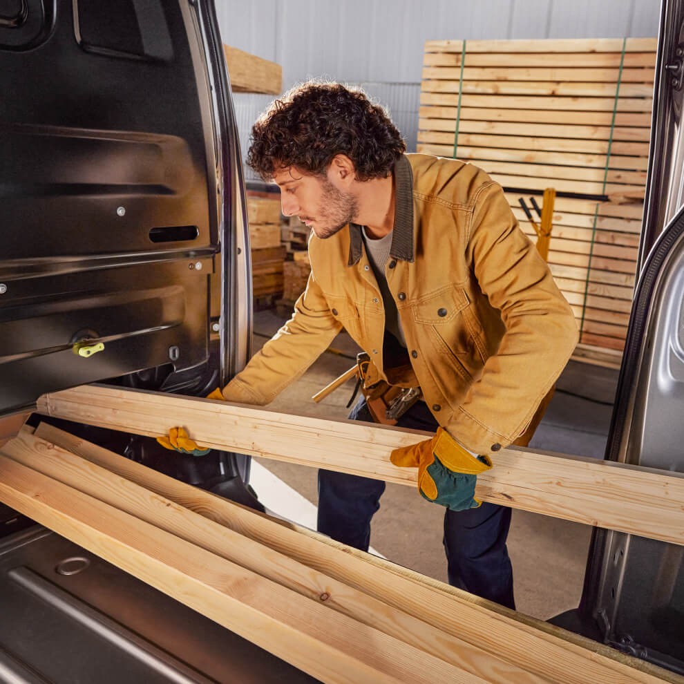 Eine Person schiebt Holzbalken in den Laderaum des Toyota Proace