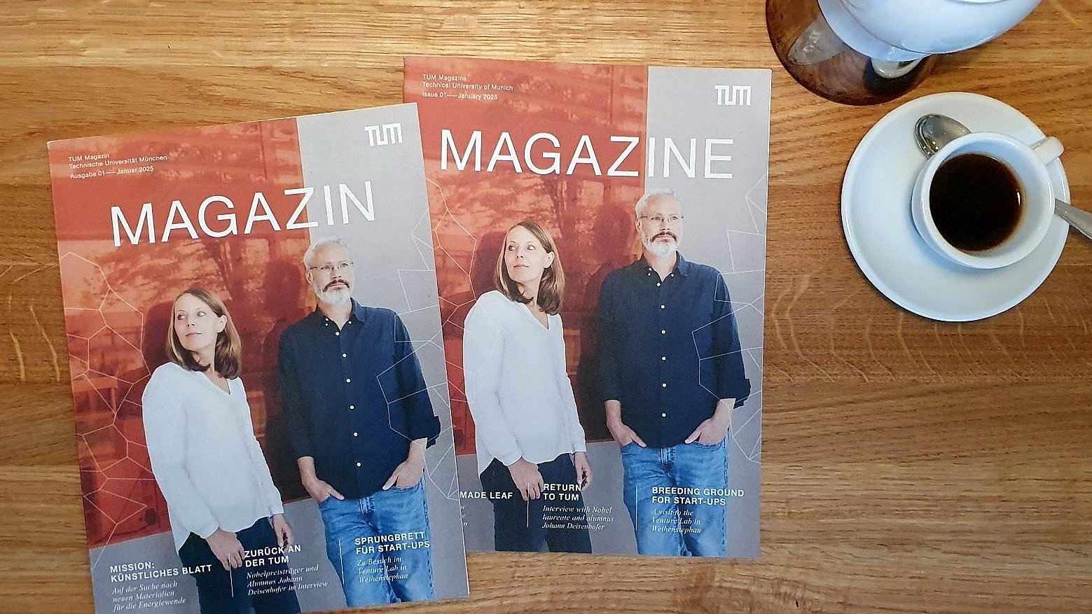 Zwei Ausgaben des neuen Magazins der Technischen Universität München (TUM) auf einem Holztisch, daneben befindet sich Kaffeegeschirr