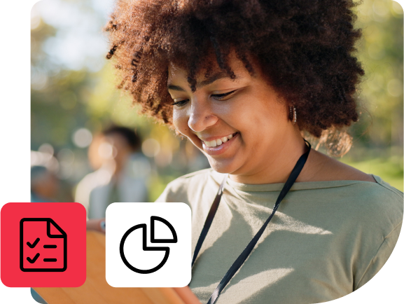 Woman with curly hair smiling and writing on a clipboard in a park.