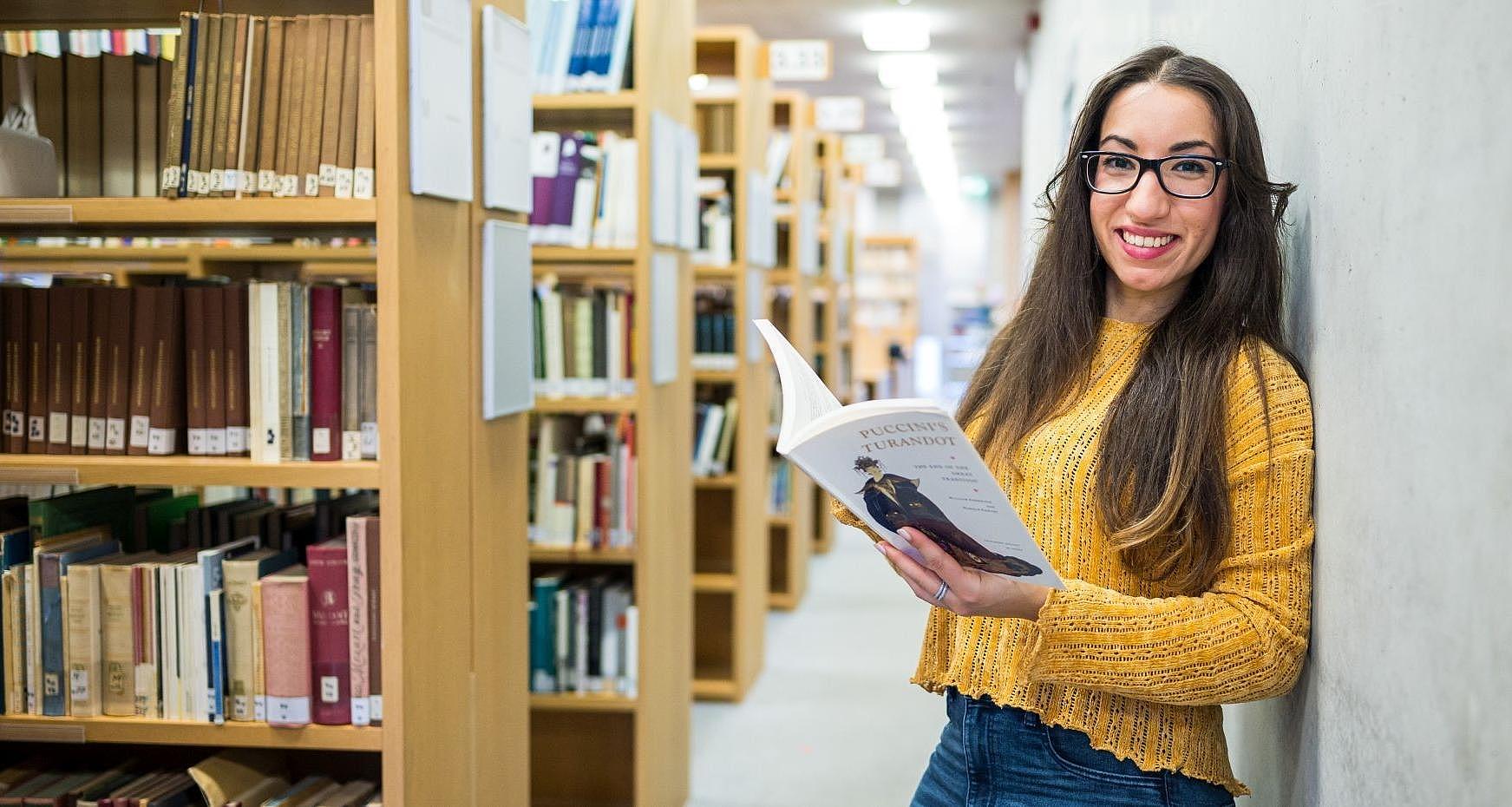 Lachende Studentin neben Bücherregalen