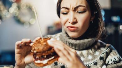 Junge Frau hält Burger in der Hand und schaut skeptisch