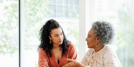 Two women seated at a table talking and holding a mobile phone.