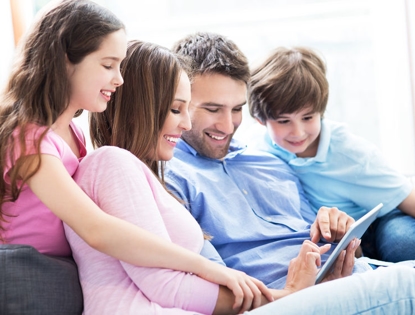 a family sitting on a couch together looking at a tablet being held by the father