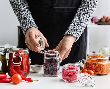 Person, die Rote Beete und andere Gemüsesorten in Einmachgläser füllt.